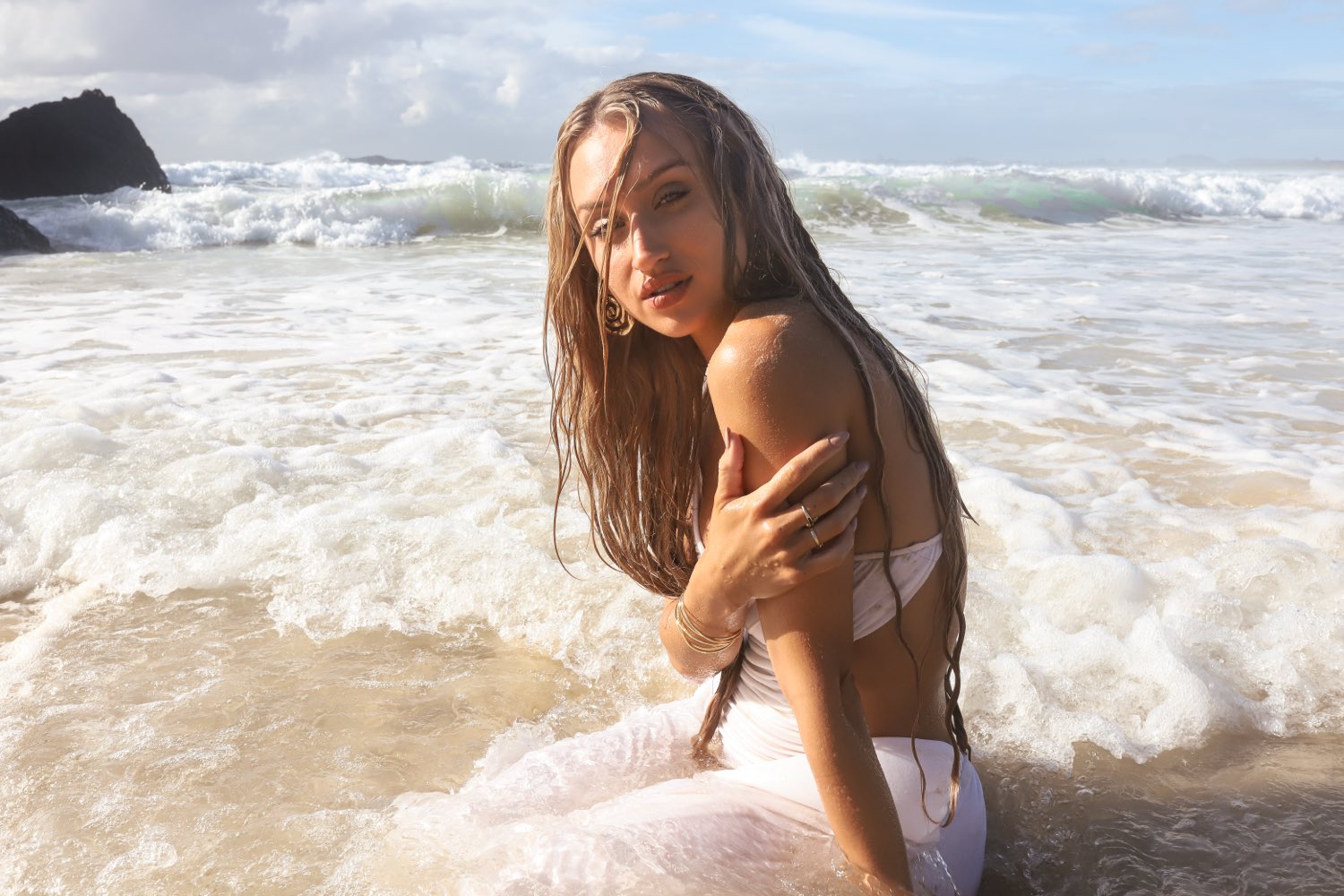 Shanti Griffin in white swimwear sitting in breaking surf, looking back over her shoulder